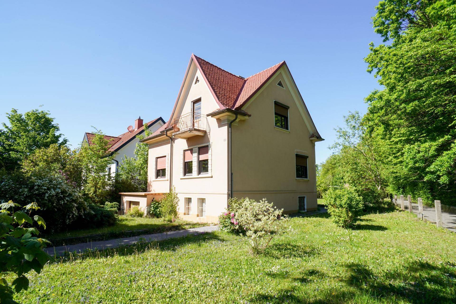 Seitenansicht des Hauses mit großem Rasenbereich und umgebenden Bäumen an einem sonnigen Tag.