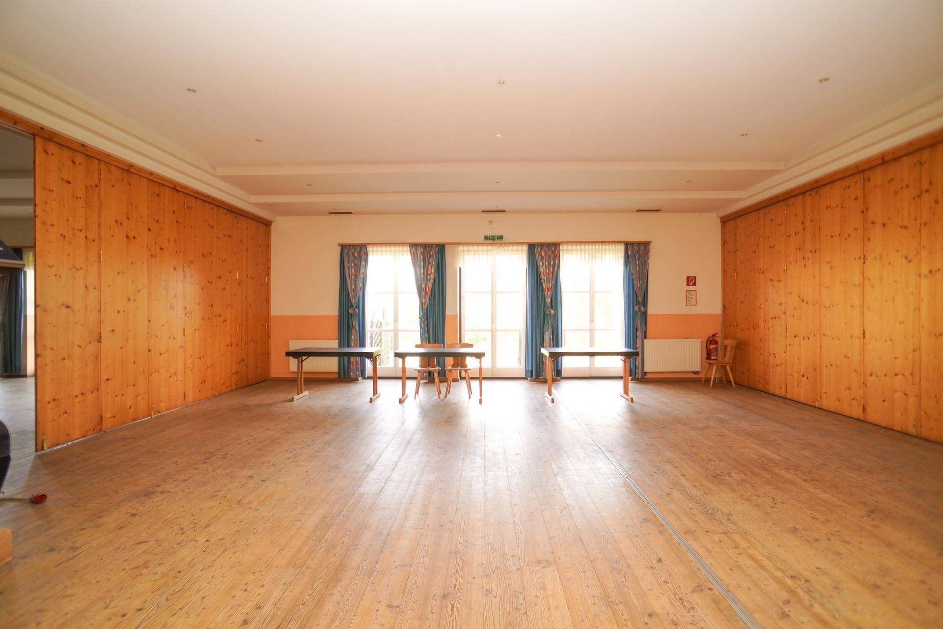 Geräumiger Saal mit Holzboden, Holzvertäfelung und hellen Fenstern.