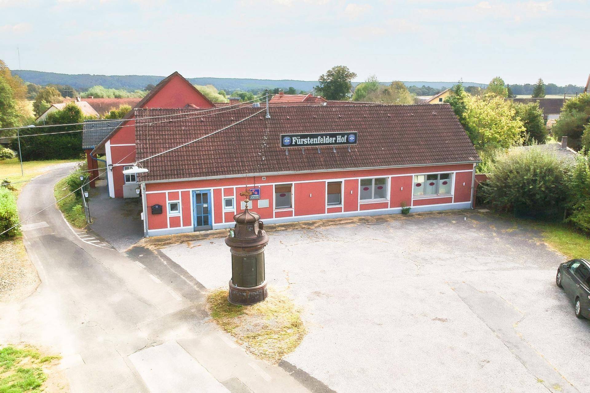 Erhöhte Ansicht des roten Gebäudes mit Parkplatz und umliegender Landschaft.