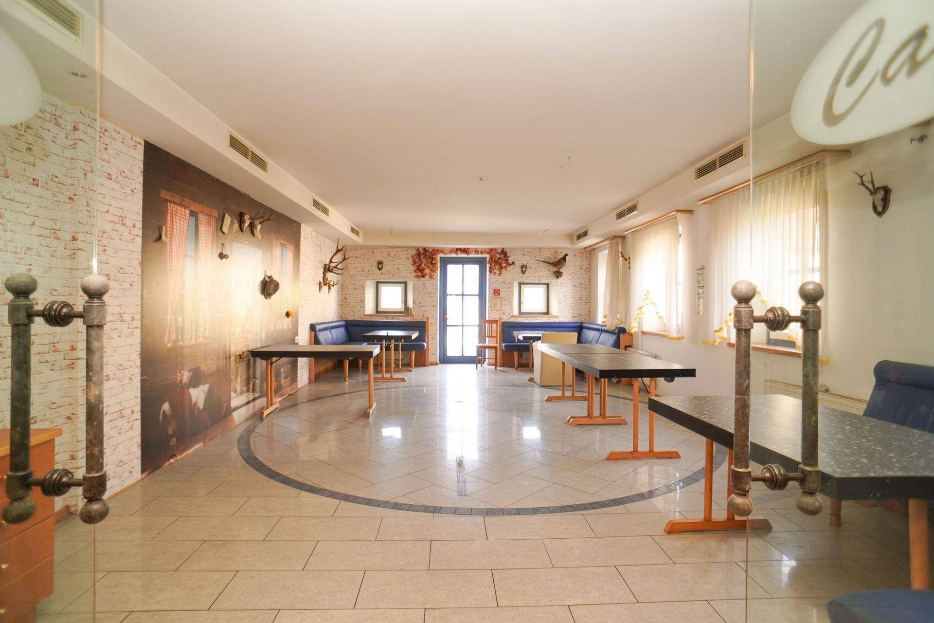Heller Veranstaltungsraum mit Fliesenboden, blauen Sitzgelegenheiten und Wanddekoration.