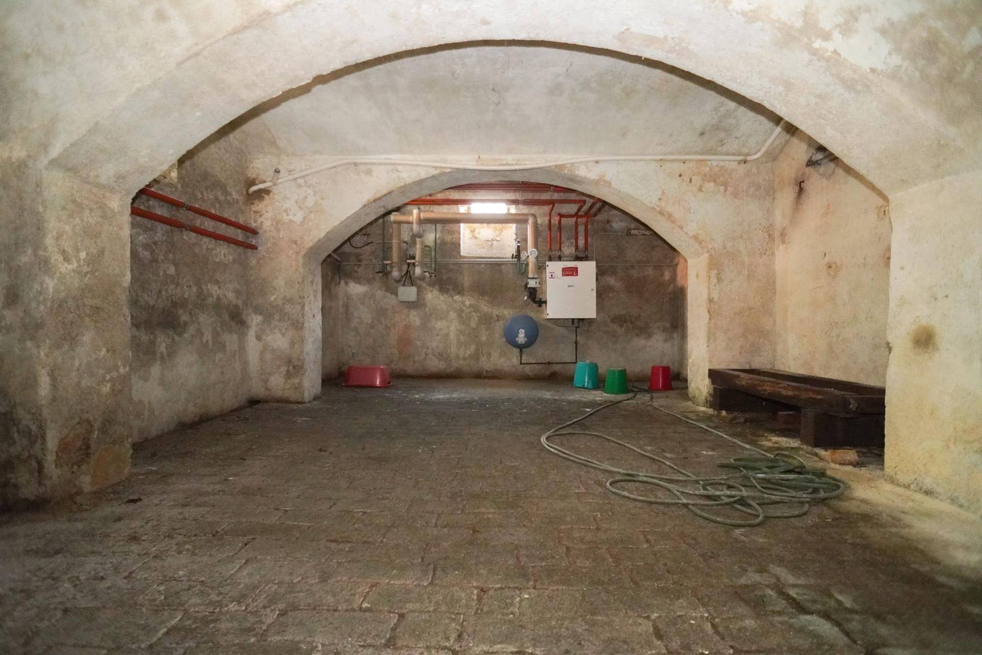 Geräumiger Gewölbekeller mit Heizungsanlage, sichtbaren Rohren und einem kleinen Fenster.