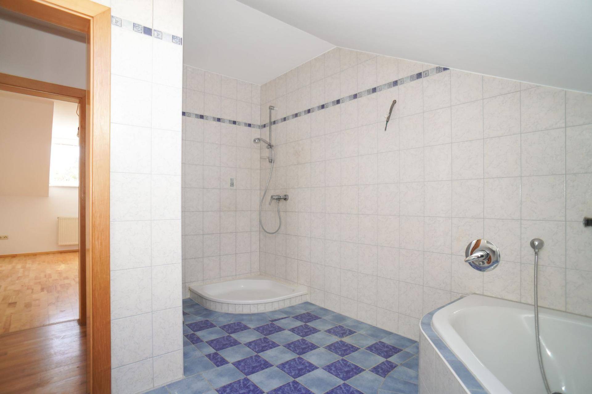 Dachbadezimmer mit Fliesenboden, Dusche und Badewanne unter der Dachschräge.