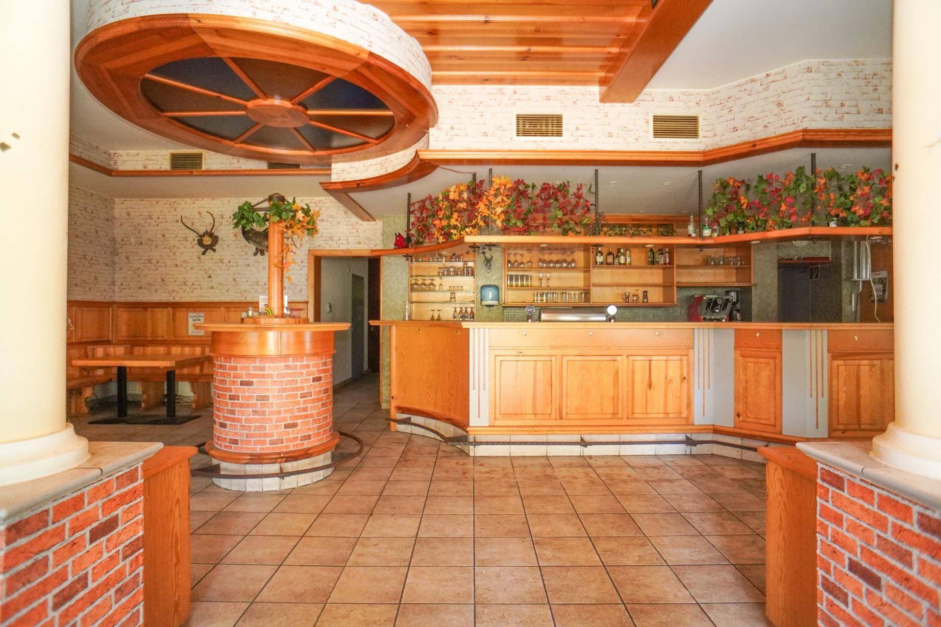 Geräumiger Gastraum mit Theke, Holzelementen und Fliesenboden im traditionellen Stil.