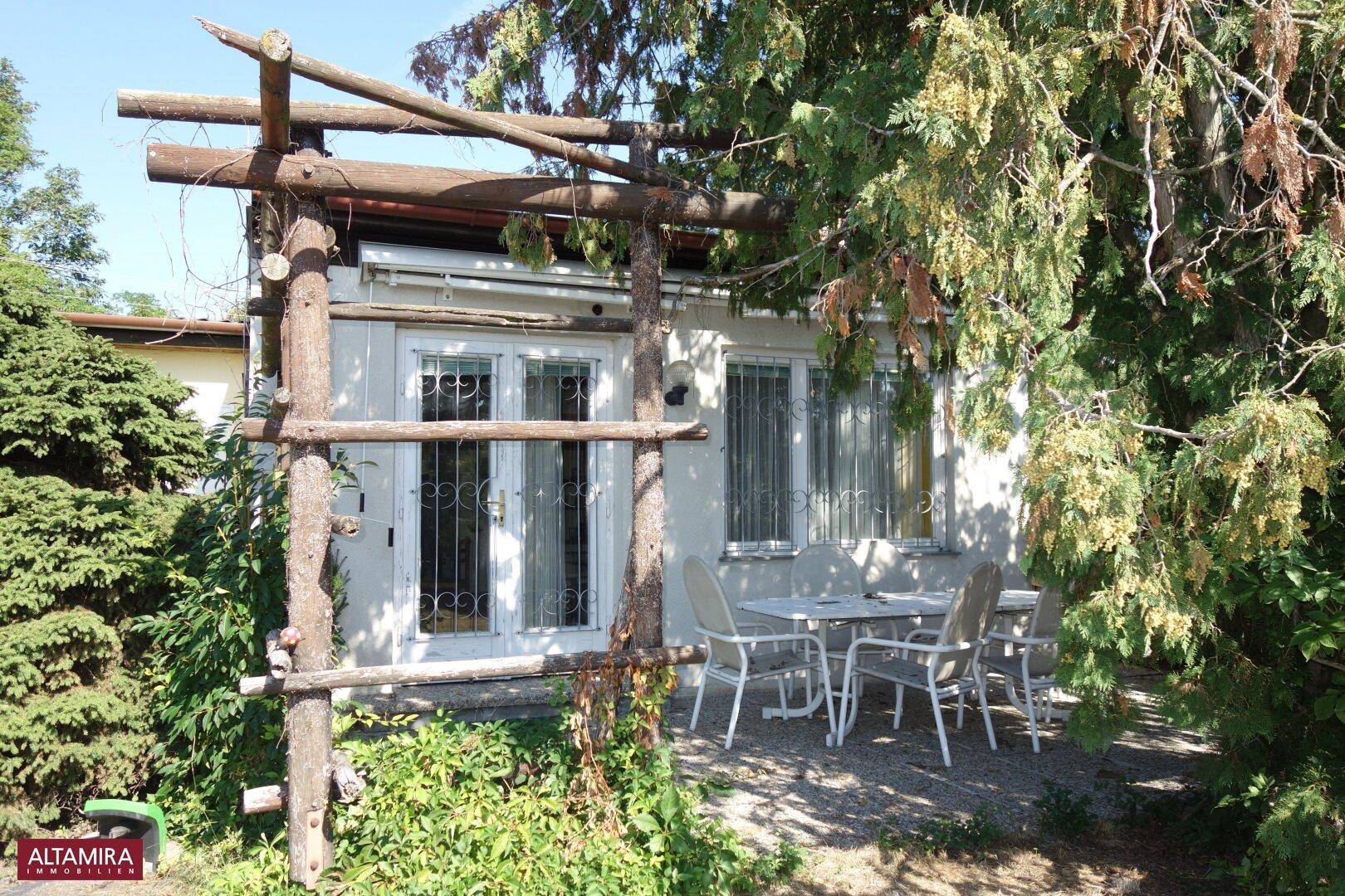 Gemütliche überdachte Terrasse mit Sitzgelegenheiten und üppigem Grün im Gartenbereich.