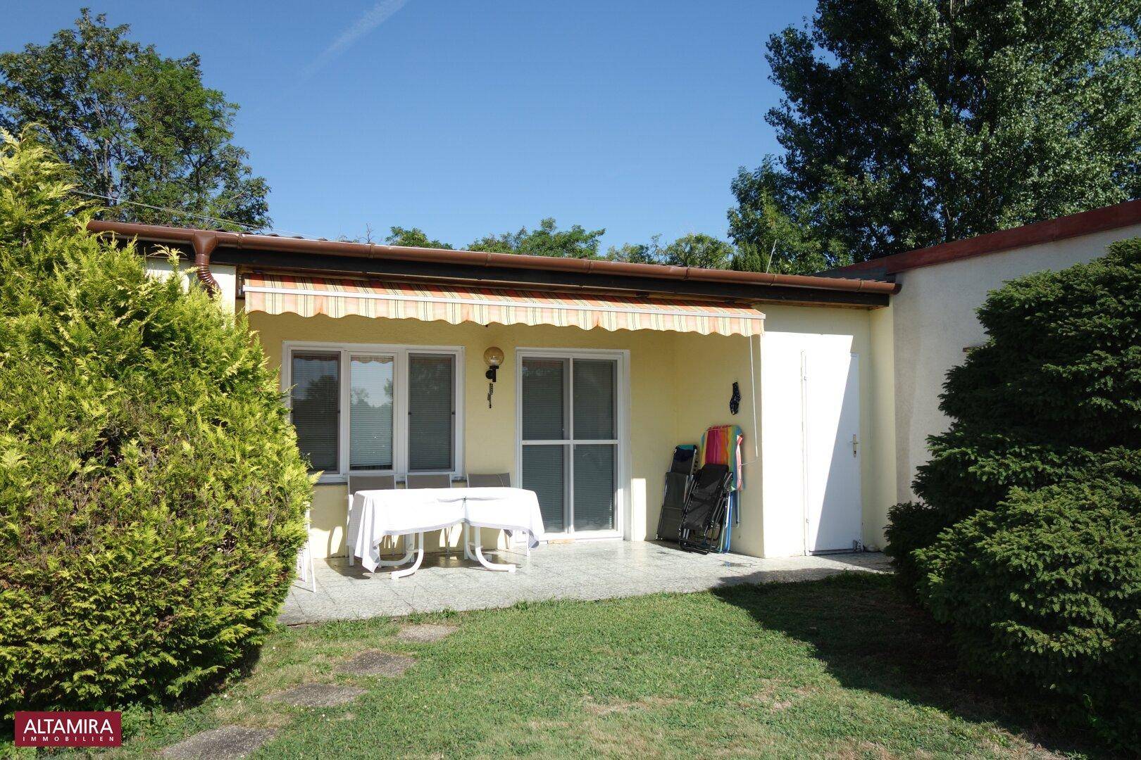Kleine Terrasse mit Markise und Gartenmöbeln, angrenzend an einen gepflegten Rasen.