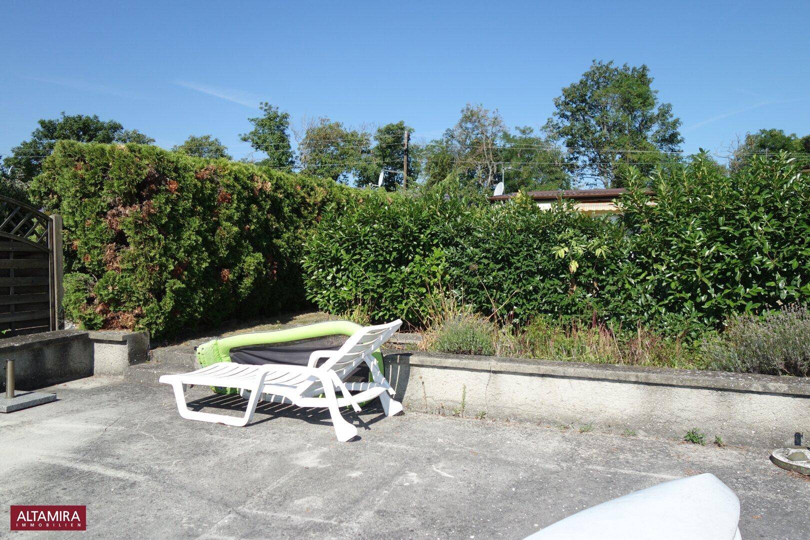 Gepflasterter Terrassenbereich mit Liegestuhl und hohen grünen Hecken im Hintergrund.