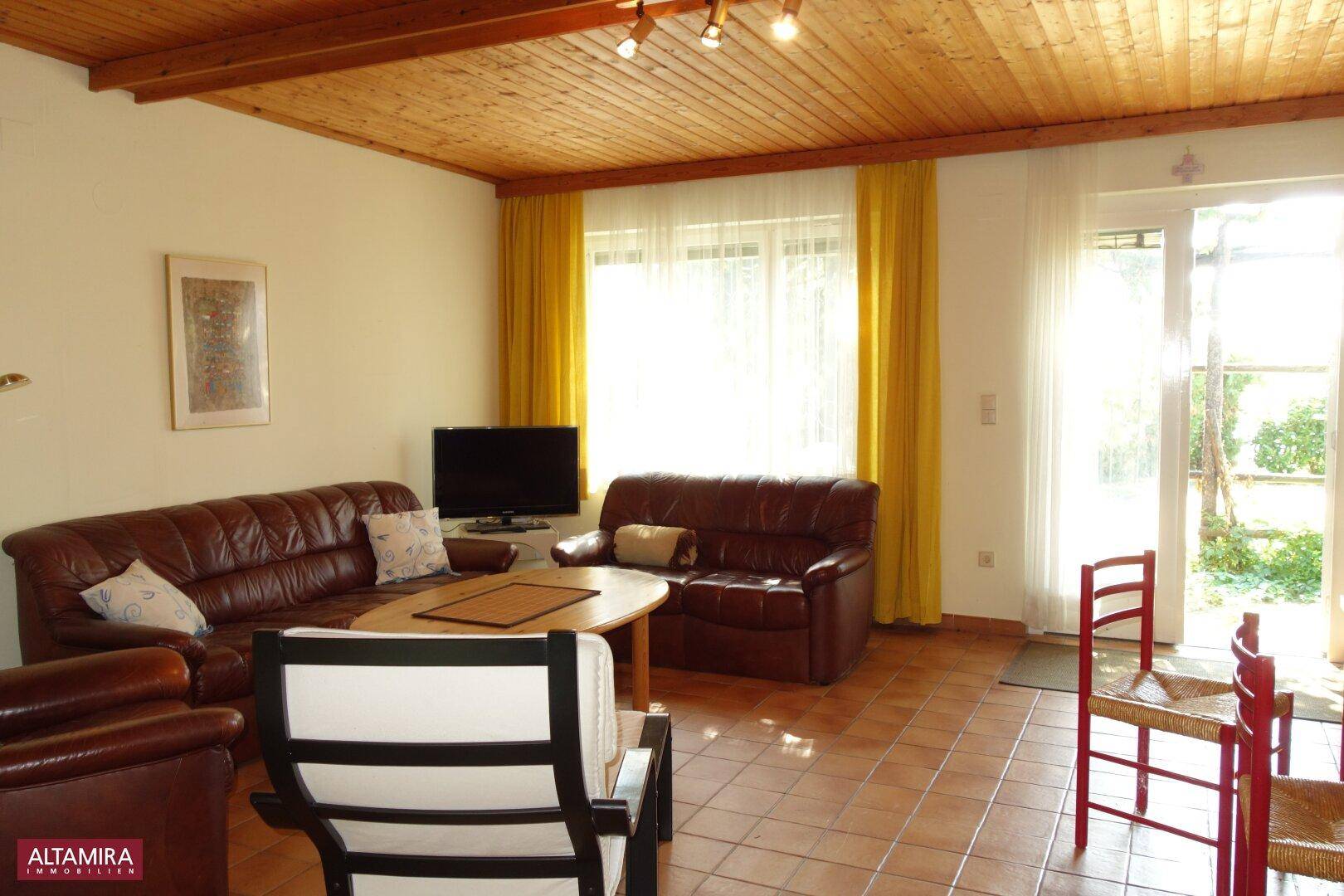 Geräumiges Wohnzimmer mit Ledersofas, Holzbalkendecke und Zugang zum Garten.