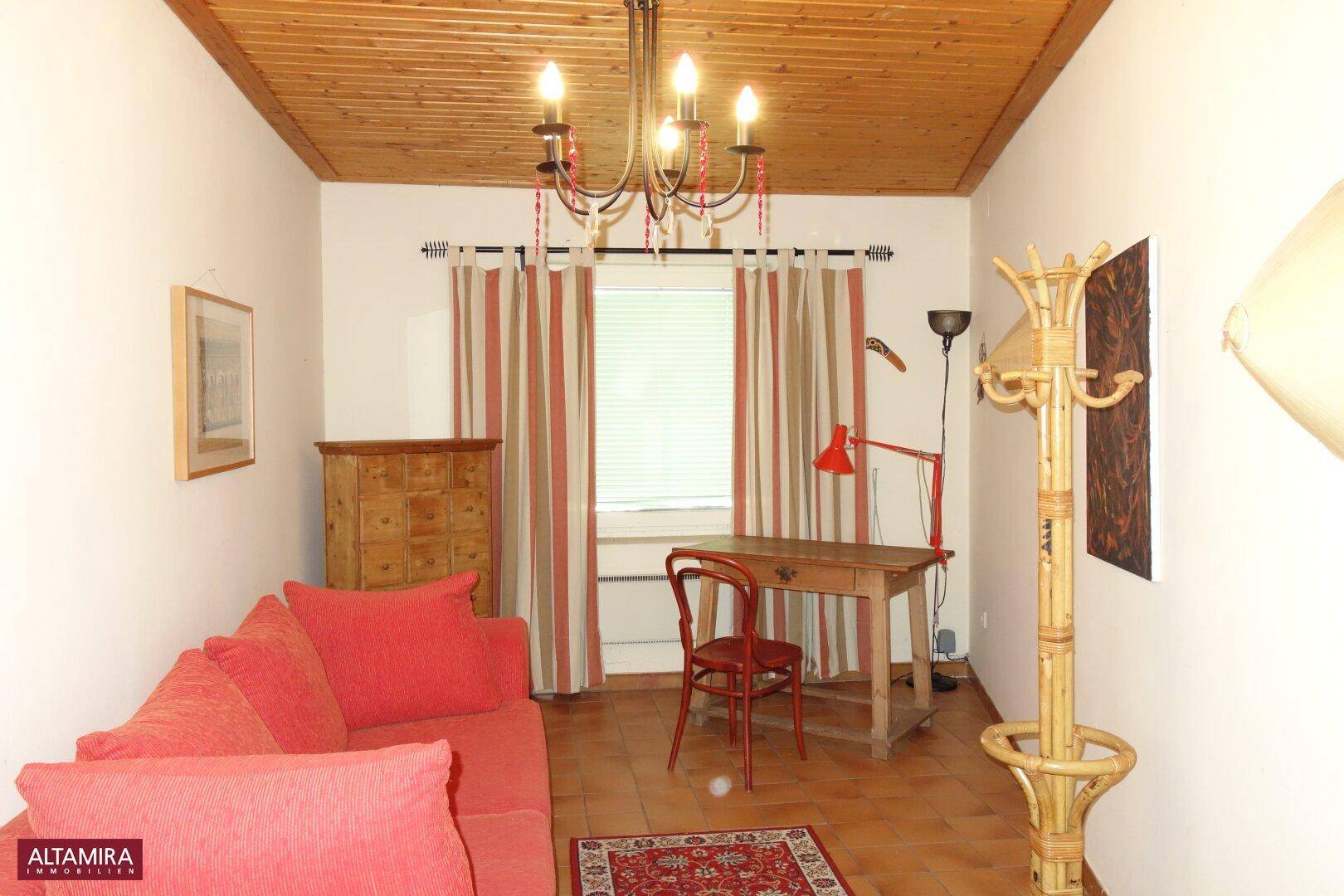 Arbeitszimmer mit rotem Sofa, Schreibtisch und Holzbalkendecke, ideal für Home-Office.