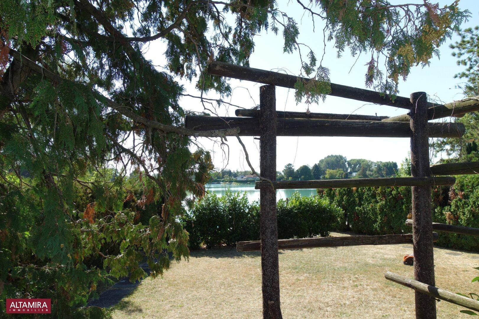 Gartenbereich mit Holzpergola und weitem Blick auf den See im Hintergrund.