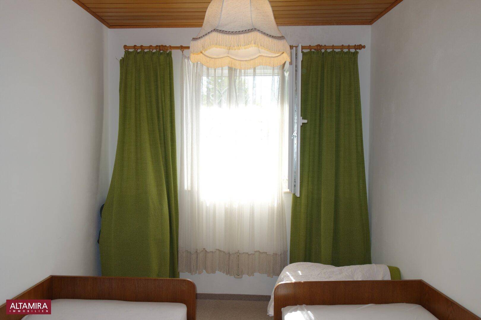 Schlafzimmer mit zwei Einzelbetten, grünen Vorhängen und Holzdeckenverkleidung.