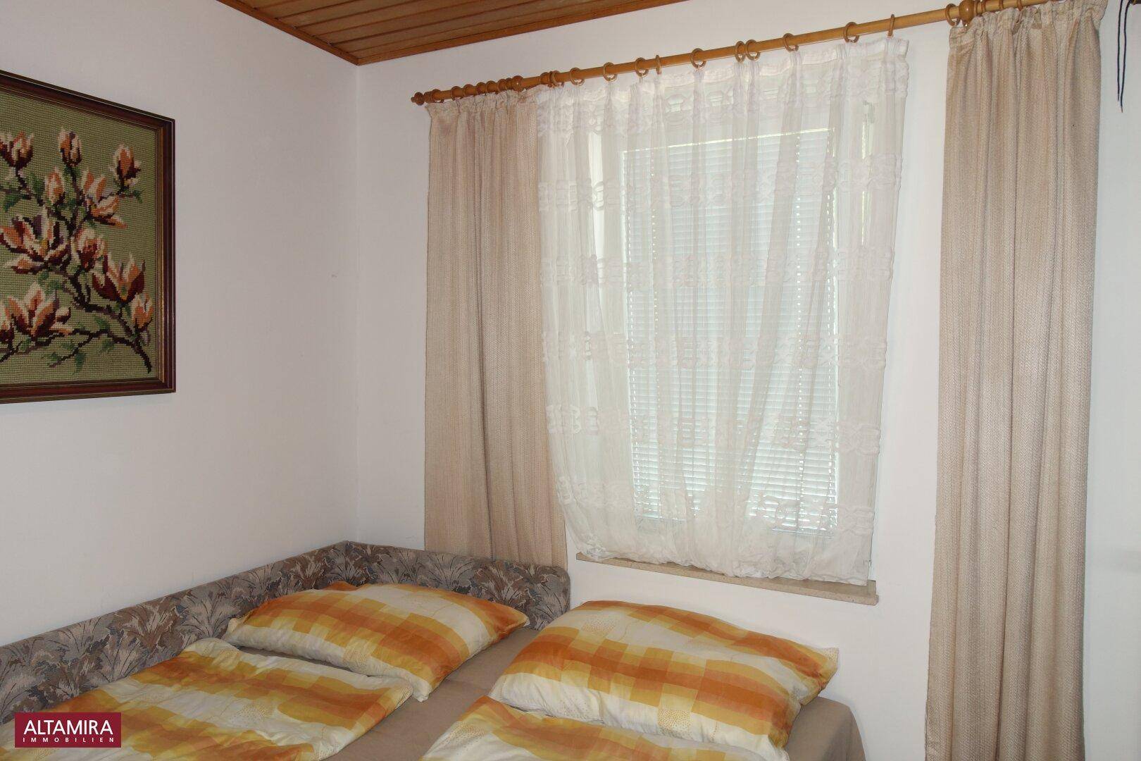 Gemütliches Schlafzimmer mit Einzelbett, beigen Vorhängen und Fenster.