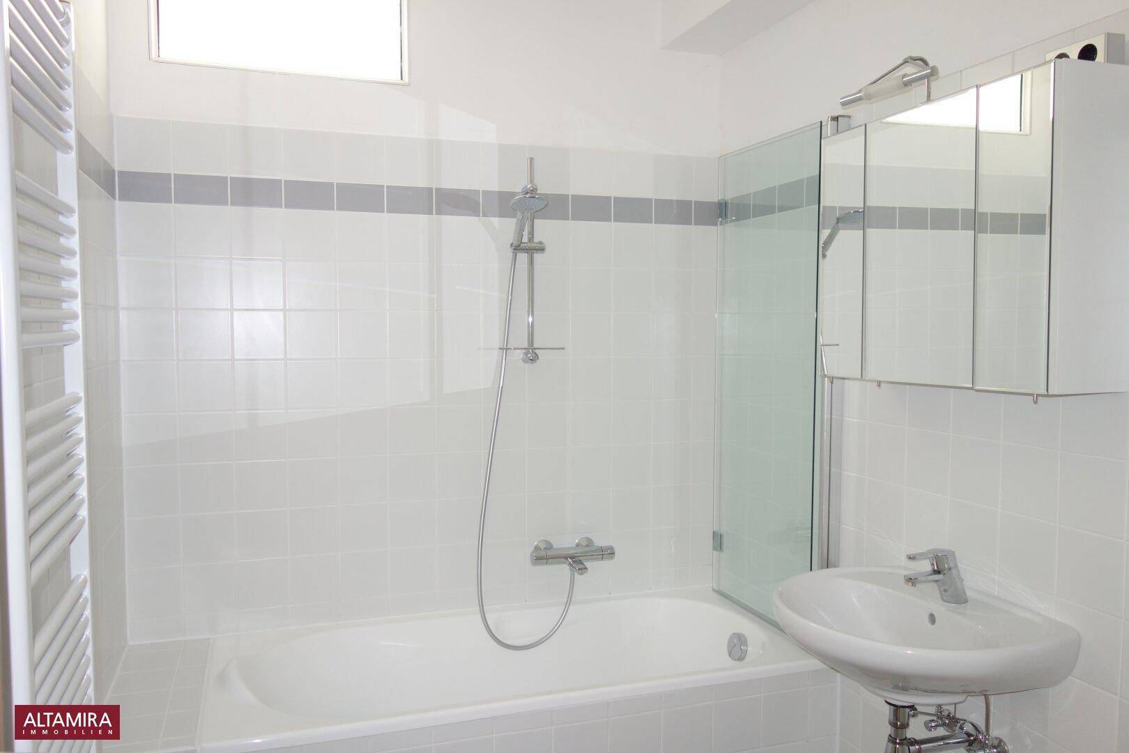 Modernes Badezimmer mit Badewanne, Dusche und weiß gefliesten Wänden mit grauer Akzentleiste.