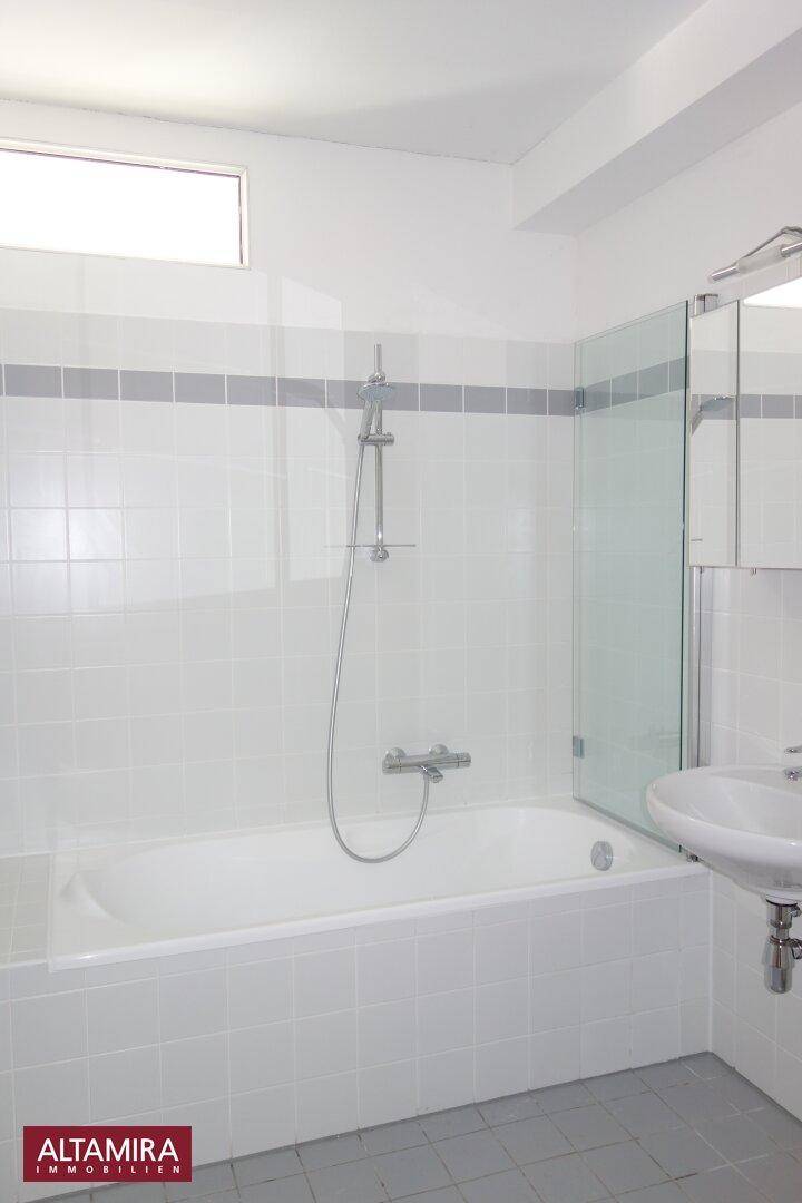 Badezimmer mit Badewanne, Duschabtrennung und weiß-grauen Fliesen, die ein sauberes Ambiente schaffen.