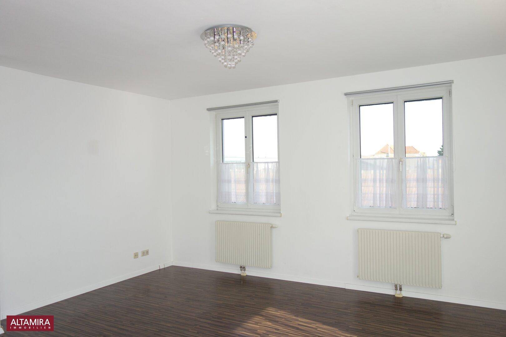 Geräumiges Zimmer mit zwei Fenstern, dunklem Laminatboden und viel natürlichem Lichteinfall.