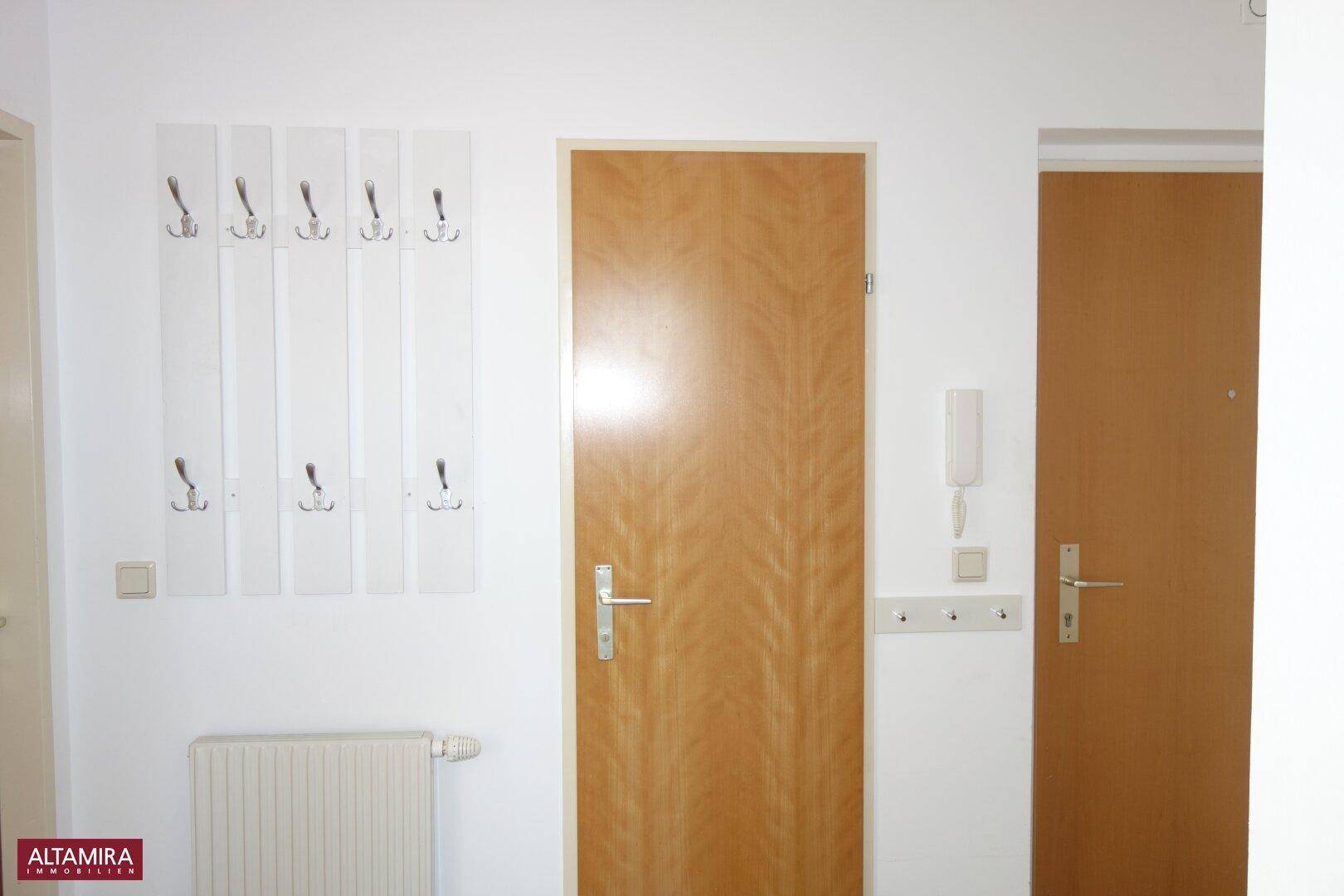 Eingangsbereich mit Garderobe, Holztür und Gegensprechanlage, der einladend wirkt.
