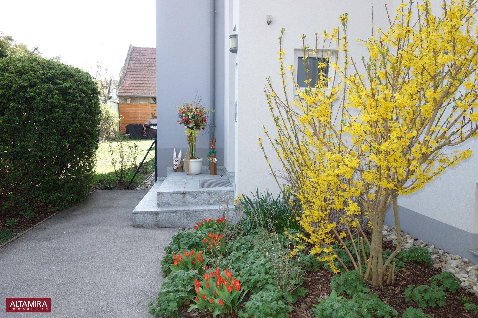 Eingangsbereich des Hauses mit blühenden Pflanzen und einem gepflegten Vorgarten.