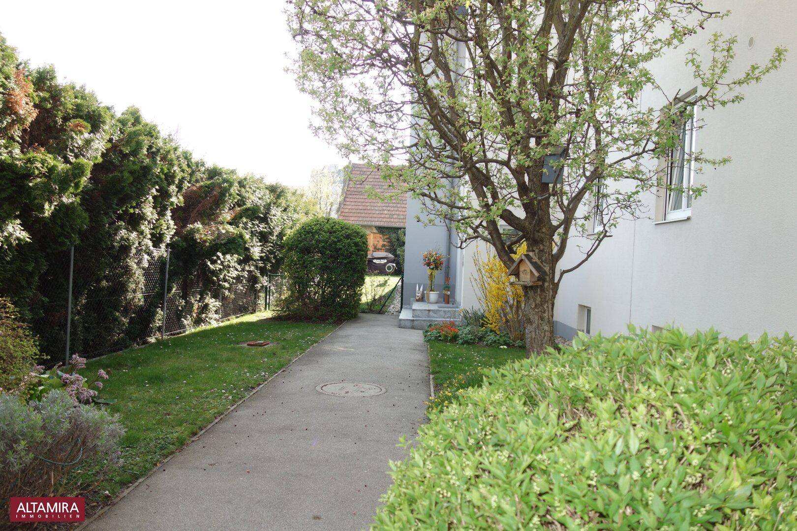 Seitlicher Gartenweg mit üppigem Grün und Bäumen, der eine ruhige Atmosphäre schafft.