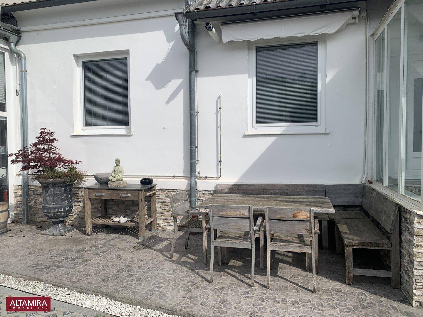 Gemütliche Außenterrasse mit Holztisch und Bänken, umgeben von einer Steinmauer und Pflanzen.