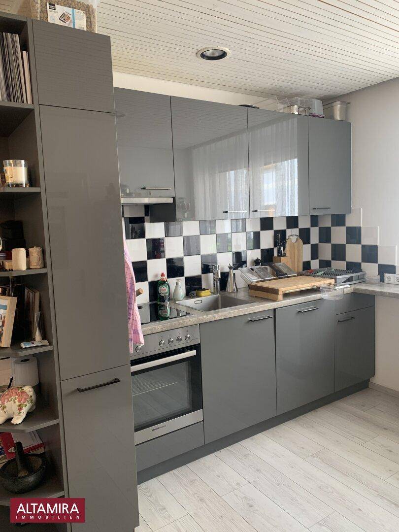 Moderne Küche mit grauen Hochglanzschränken, schwarz-weiß gefliestem Spritzschutz und Einbaugeräten.