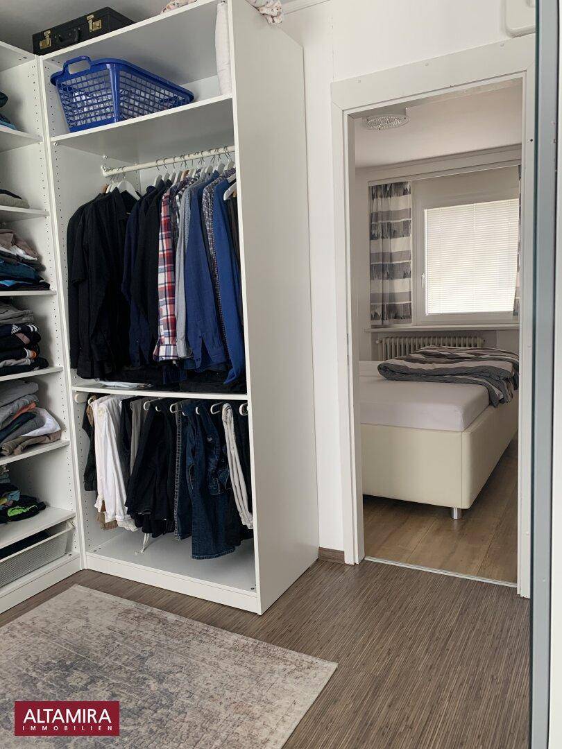 Begehbarer Kleiderschrank mit offenen Regalen und Kleiderstangen, angrenzend an ein Schlafzimmer.