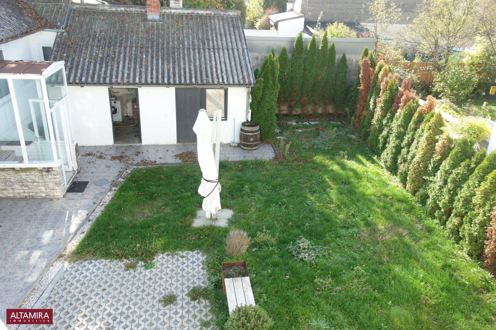Vogelperspektive auf den Gartenbereich mit Rasenfläche, Hecken und einem kleinen Nebengebäude.