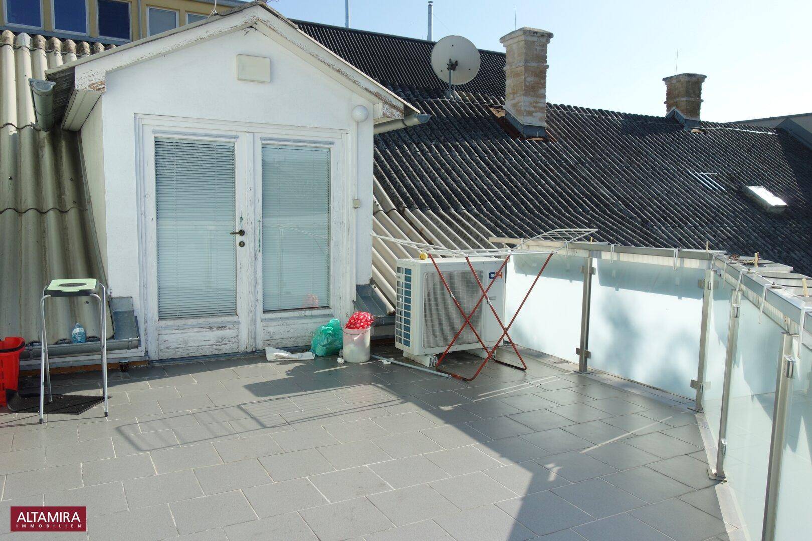Dachterrasse mit Fliesenboden, Glasgeländer und einer Klimaanlage im Freien.