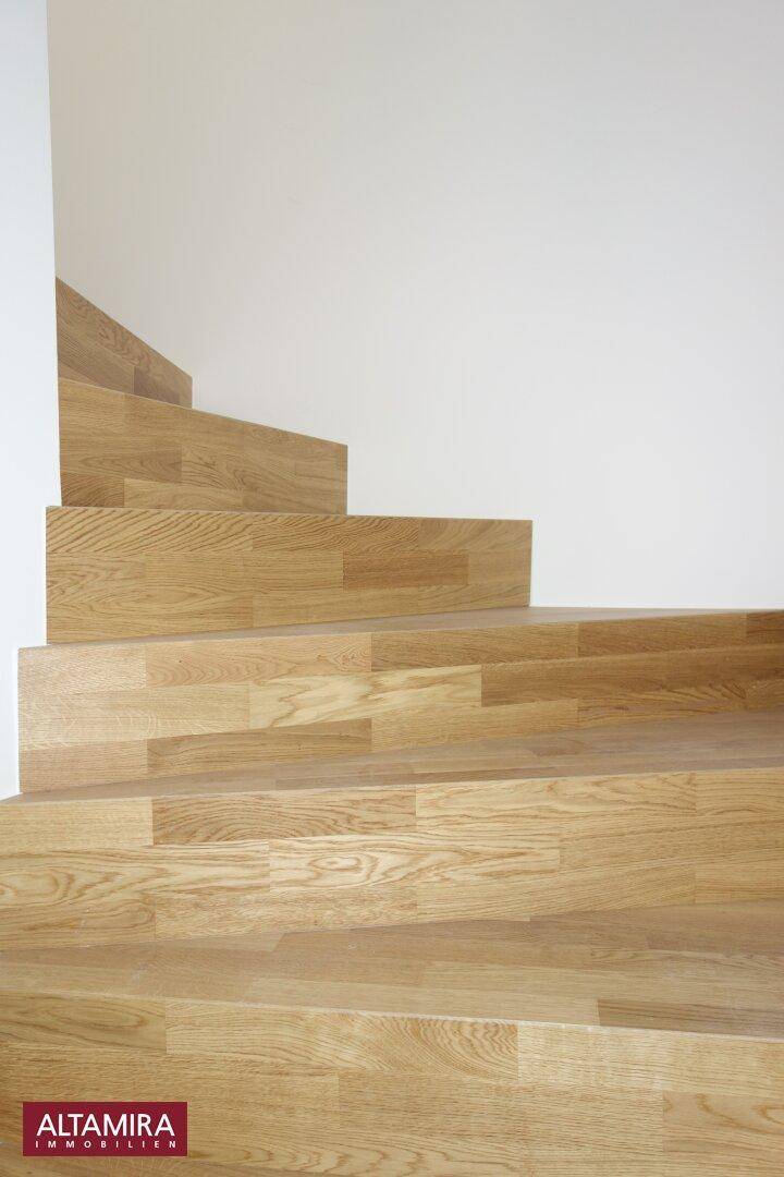 Moderne Holztreppe mit hellen Stufen und klaren Linien, die verschiedene Ebenen verbindet.