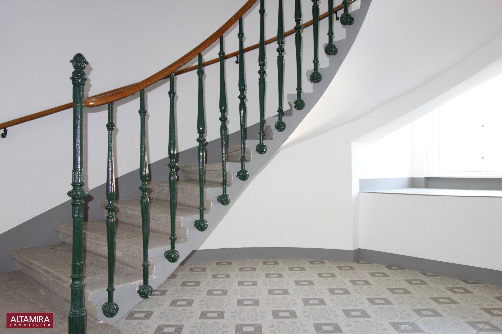 Elegantes Treppenhaus mit geschwungenem Geländer, verzierten Balustern und gemusterten Bodenfliesen.