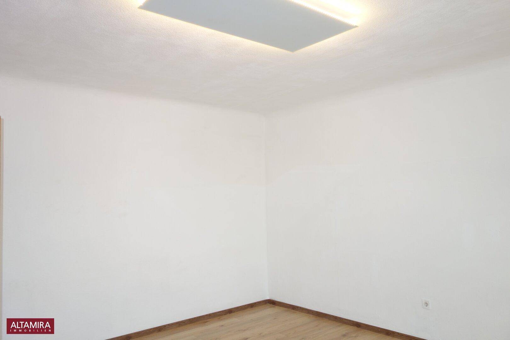 Leerer Raum mit weiß gestrichenen Wänden und einfacher Deckenbeleuchtung, bereit zur individuellen Gestaltung.