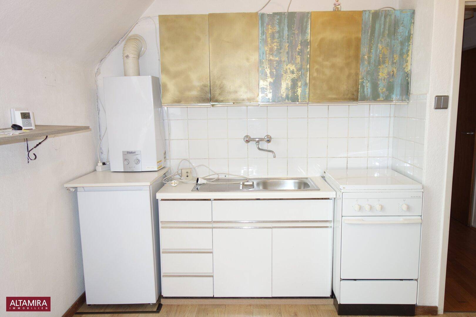 Einfache Küchenzeile mit Spüle, Herd und Kühlschrank unter einer Dachschräge.