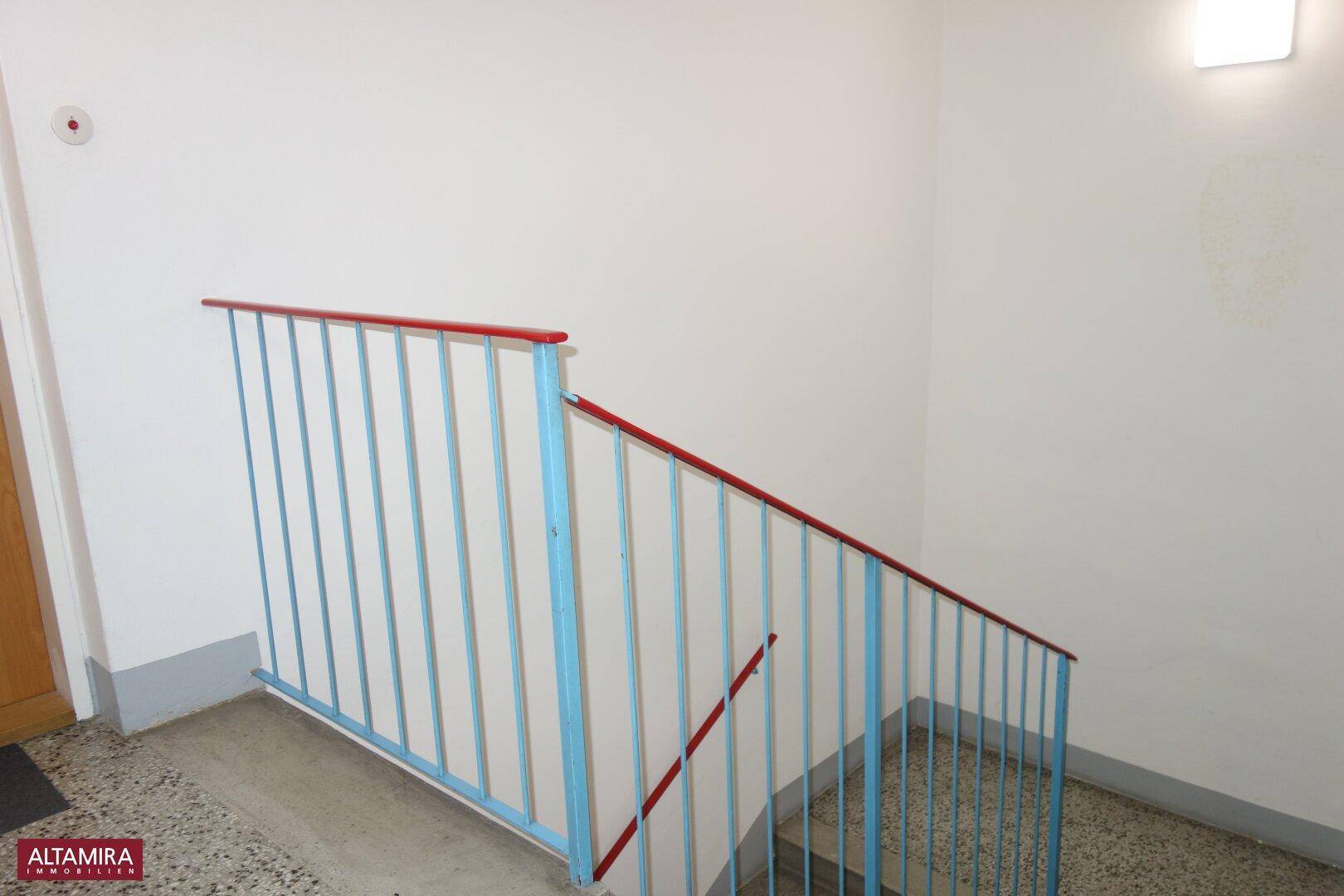 Treppenhaus mit farbigen Geländern und Terrazzoboden in einem Mehrfamilienhaus.