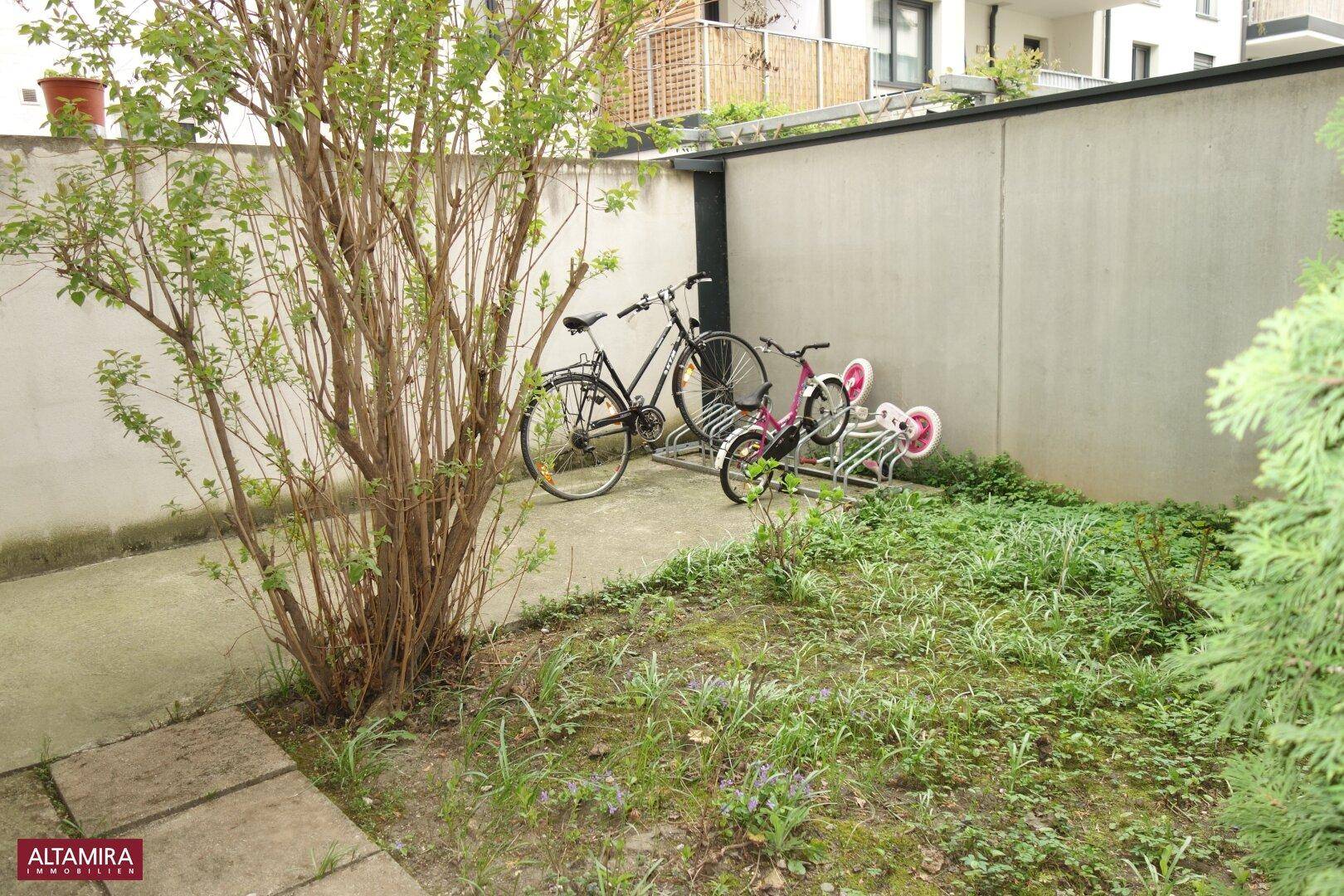 Gemeinschaftsgartenbereich mit Fahrradständern, Sträuchern und Grünflächen.