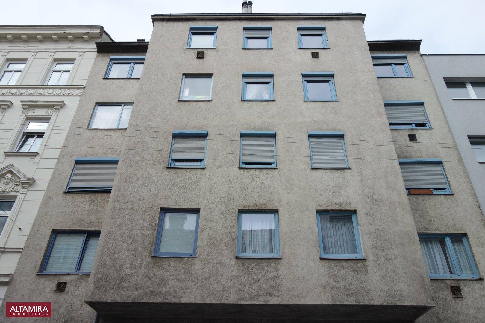 Mehrstöckiges Wohngebäude mit zahlreichen Fenstern und Rollläden an der Fassade.