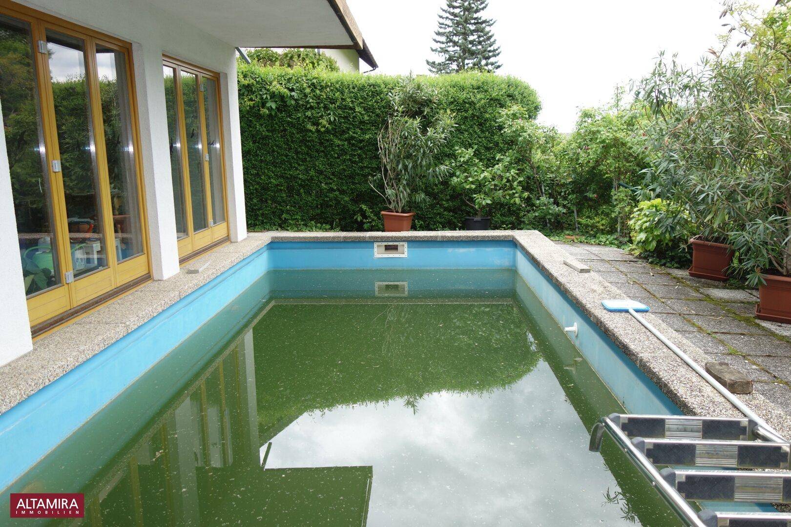 Außenpool im Gartenbereich mit angrenzender Terrasse und umgebender Hecke.