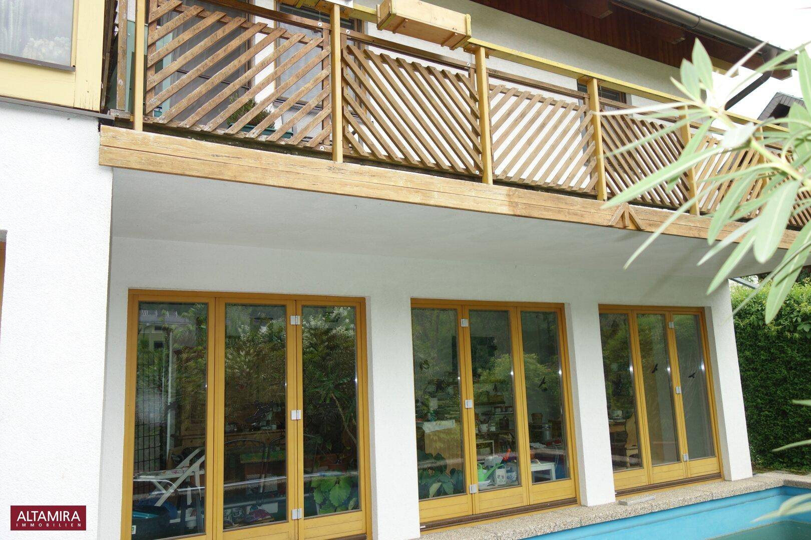 Holzverkleideter Balkon über großen Fenstern, der einen Blick ins Grüne bietet.