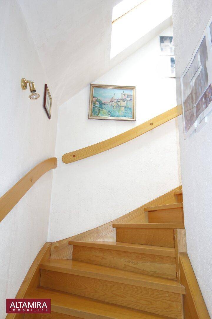 Helles Treppenhaus mit Holztreppe, Holzgeländer und einem Oberlicht für natürliches Licht.