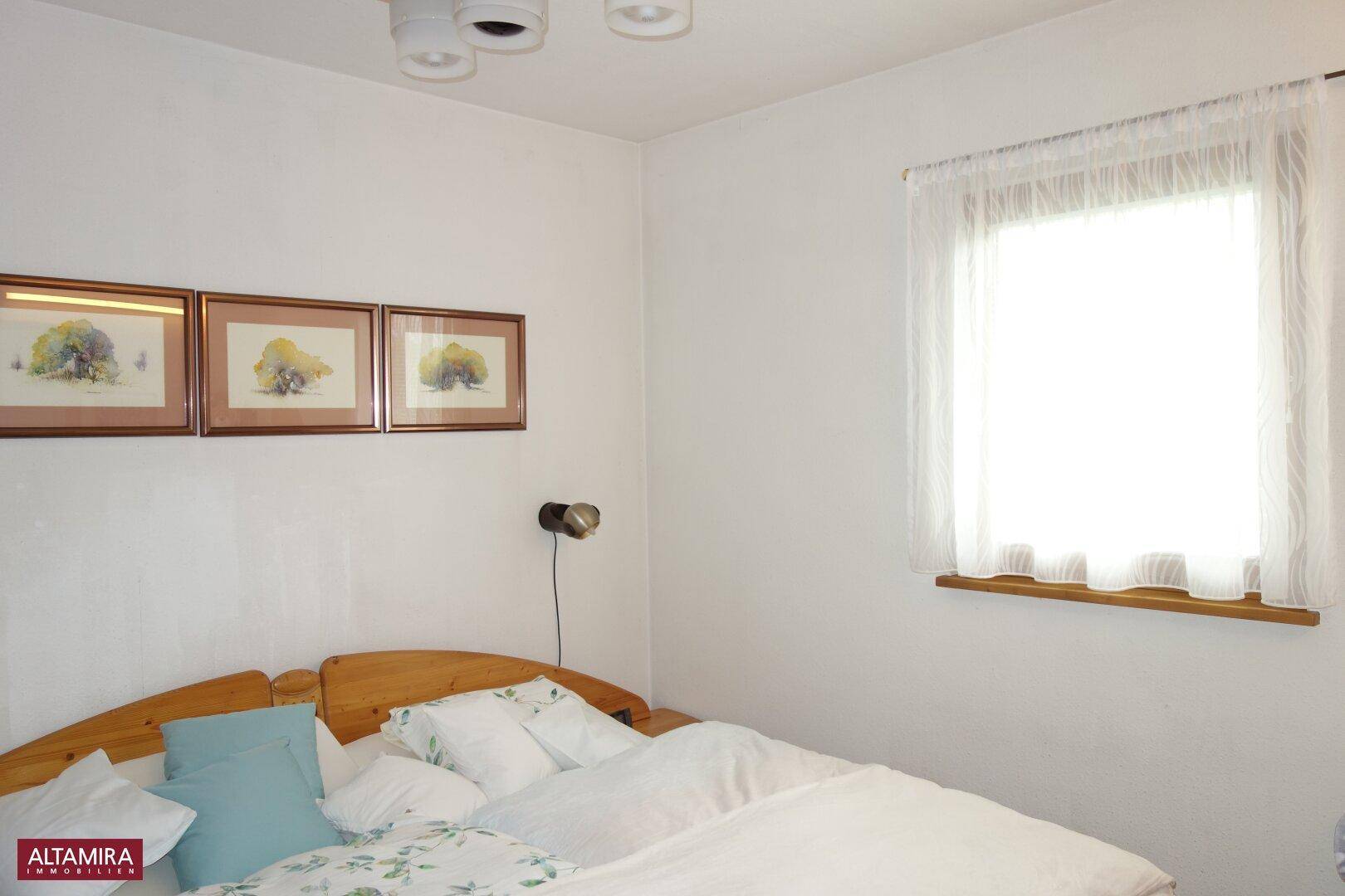 Helles Schlafzimmer mit Doppelbett, weiß gestrichenen Wänden und einem Fenster.