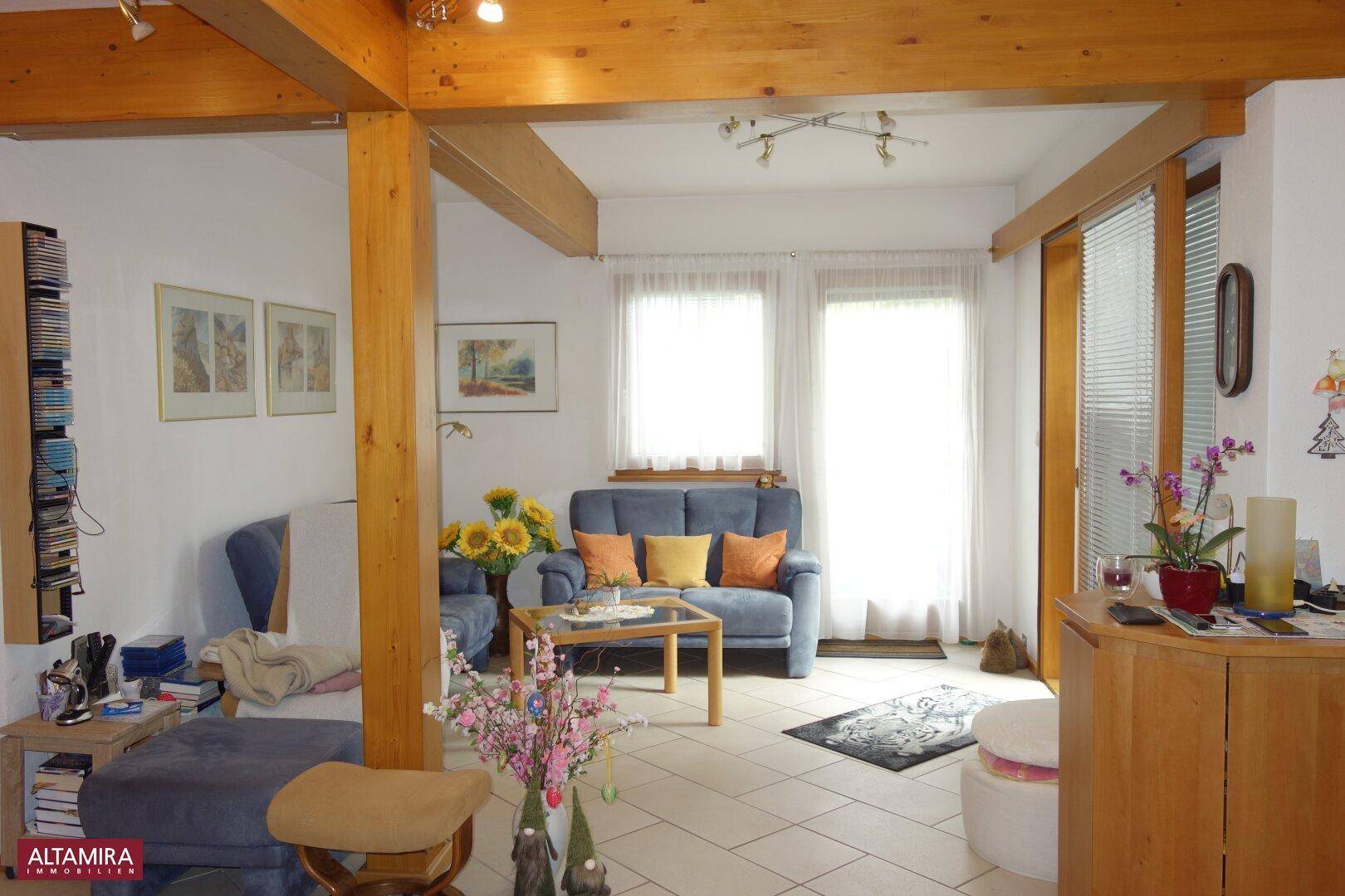 Helles Wohnzimmer mit sichtbaren Holzbalken, Fliesenboden und gemütlicher Sitzecke.