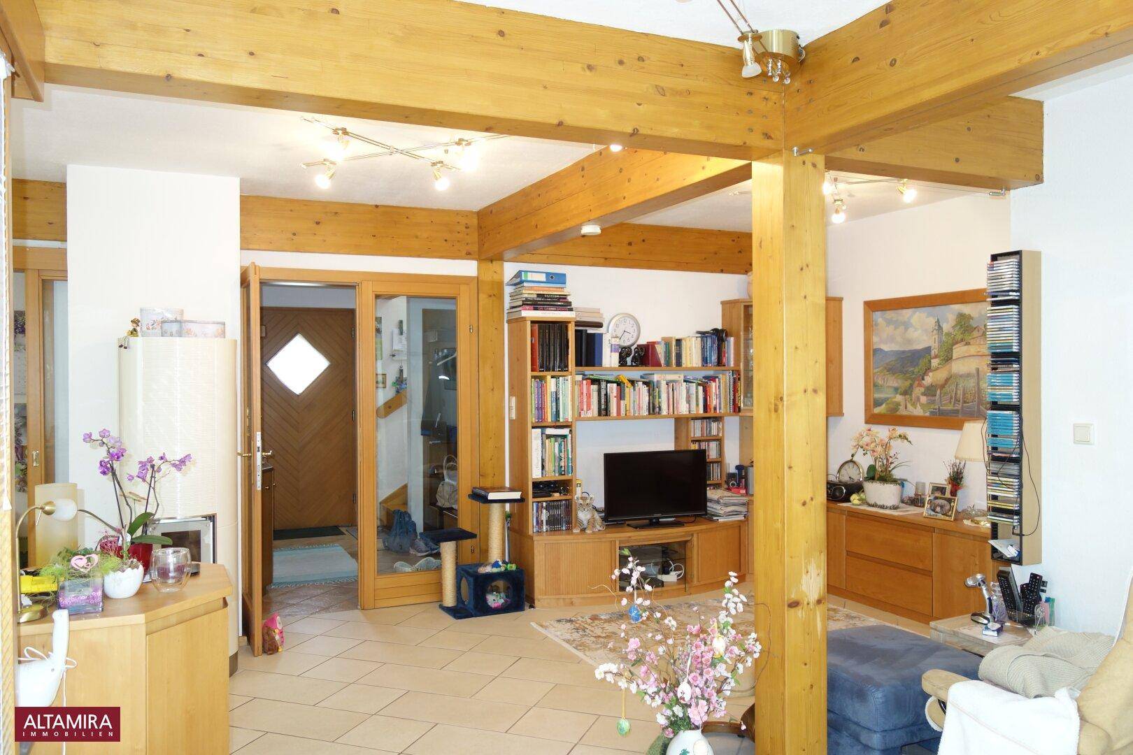 Geräumiger Wohnbereich mit Holzbalken, Fliesenboden und Blick auf den Eingangsbereich.