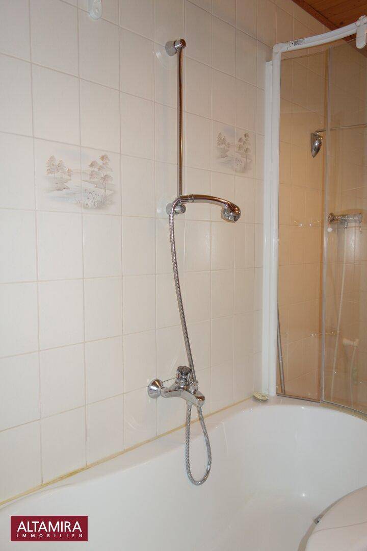 Badezimmer mit Badewanne, integrierter Dusche und hellen Fliesen an den Wänden.