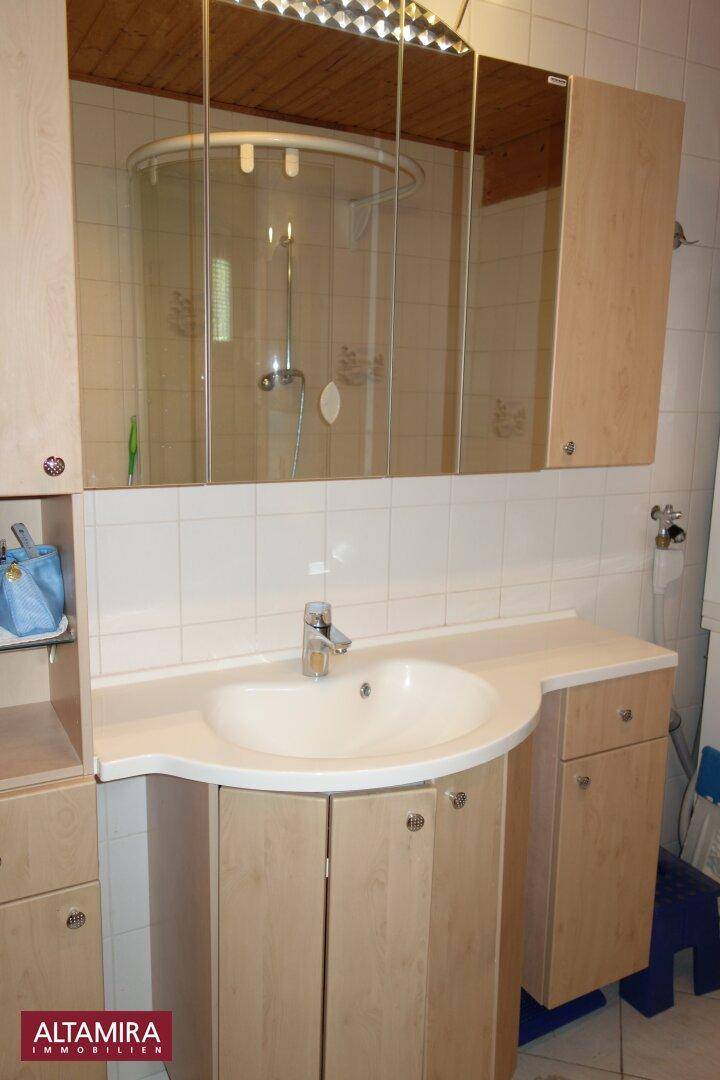 Badezimmer mit Waschtisch, Spiegelschrank und Holzunterschränken unter einer Holzdecke.