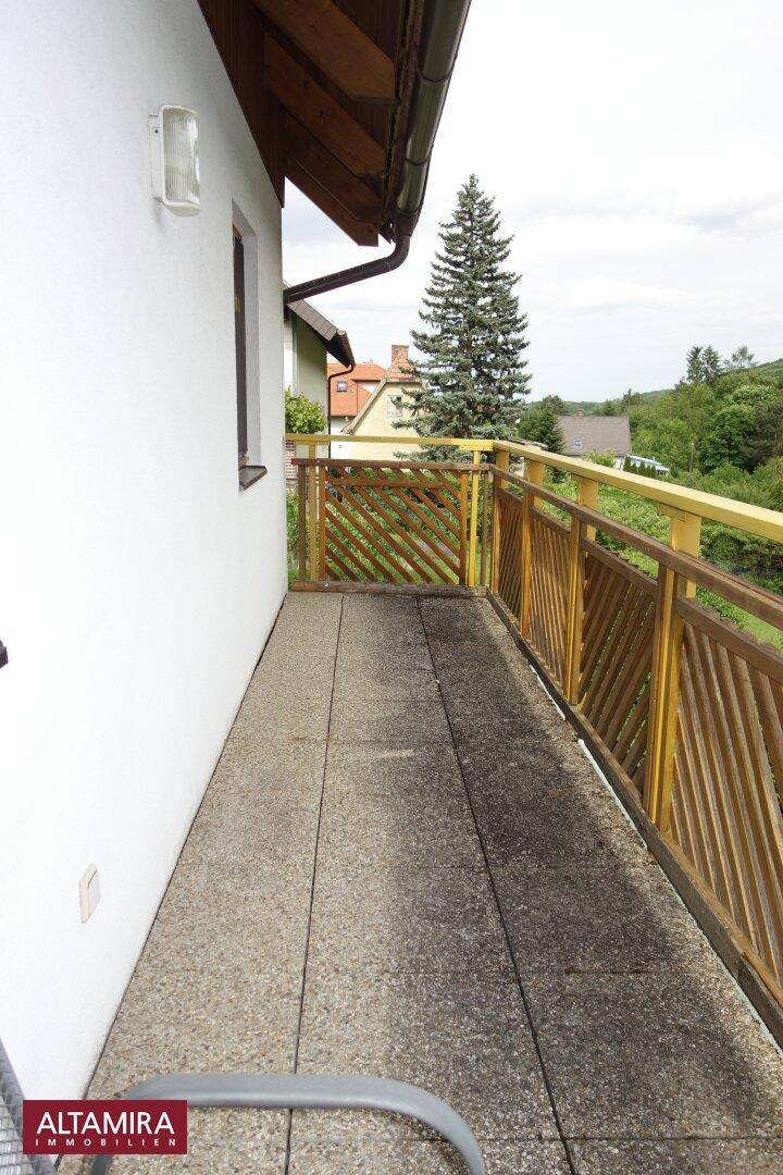 Schmaler Balkon mit Betonboden und Holzgeländer, bietet Blick auf Bäume und Häuser.