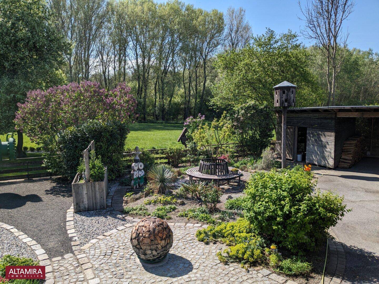 Weitläufiger Garten mit runder Baumbank, Schuppen und einem gepflasterten Bereich.