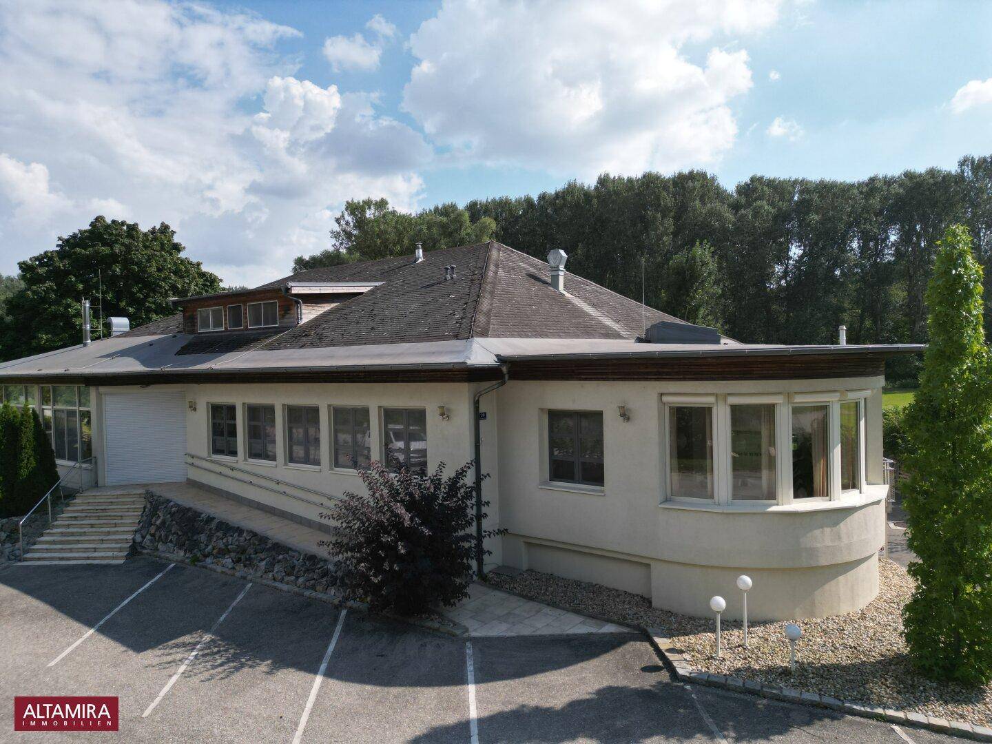Moderne Gebäudefassade mit großen Fenstern und einem gepflegten Außenbereich unter blauem Himmel.