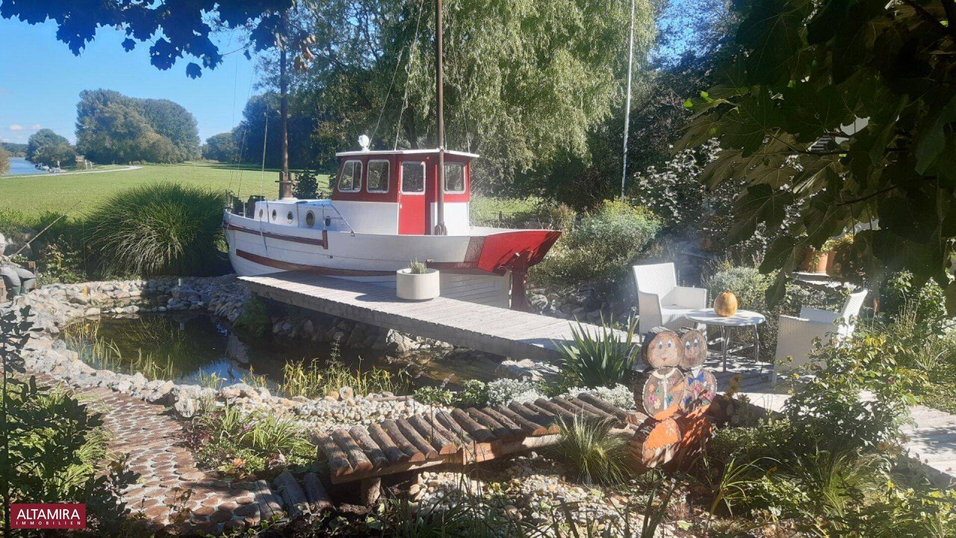 Detailansicht des Gartens mit einem dekorativen Boot, Teich und gemütlicher Sitzecke im Freien.