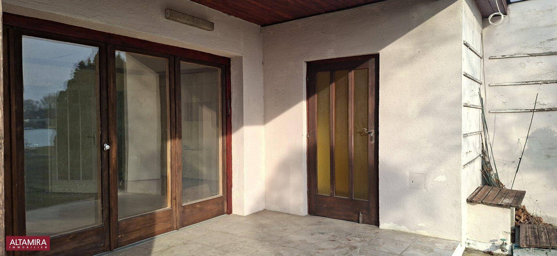 Fassade eines Gebäudes mit großen Glastüren und einer Holztür, die auf eine Terrasse führen.