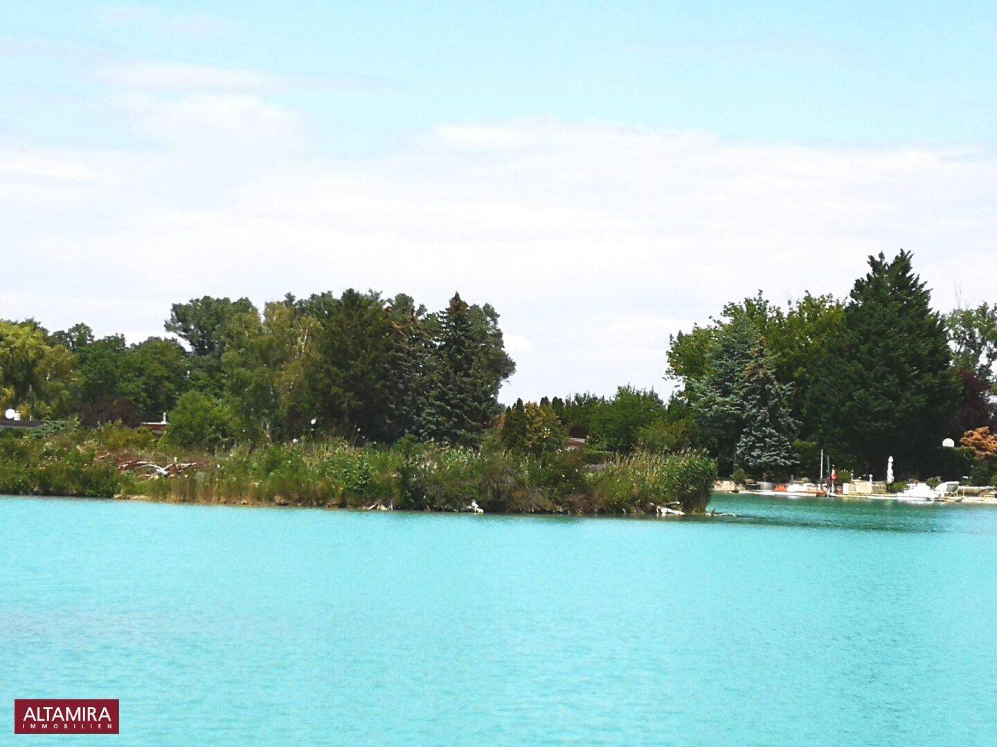 Breiter Blick auf einen blauen See mit üppig bewachsenem Ufer und Bäumen.