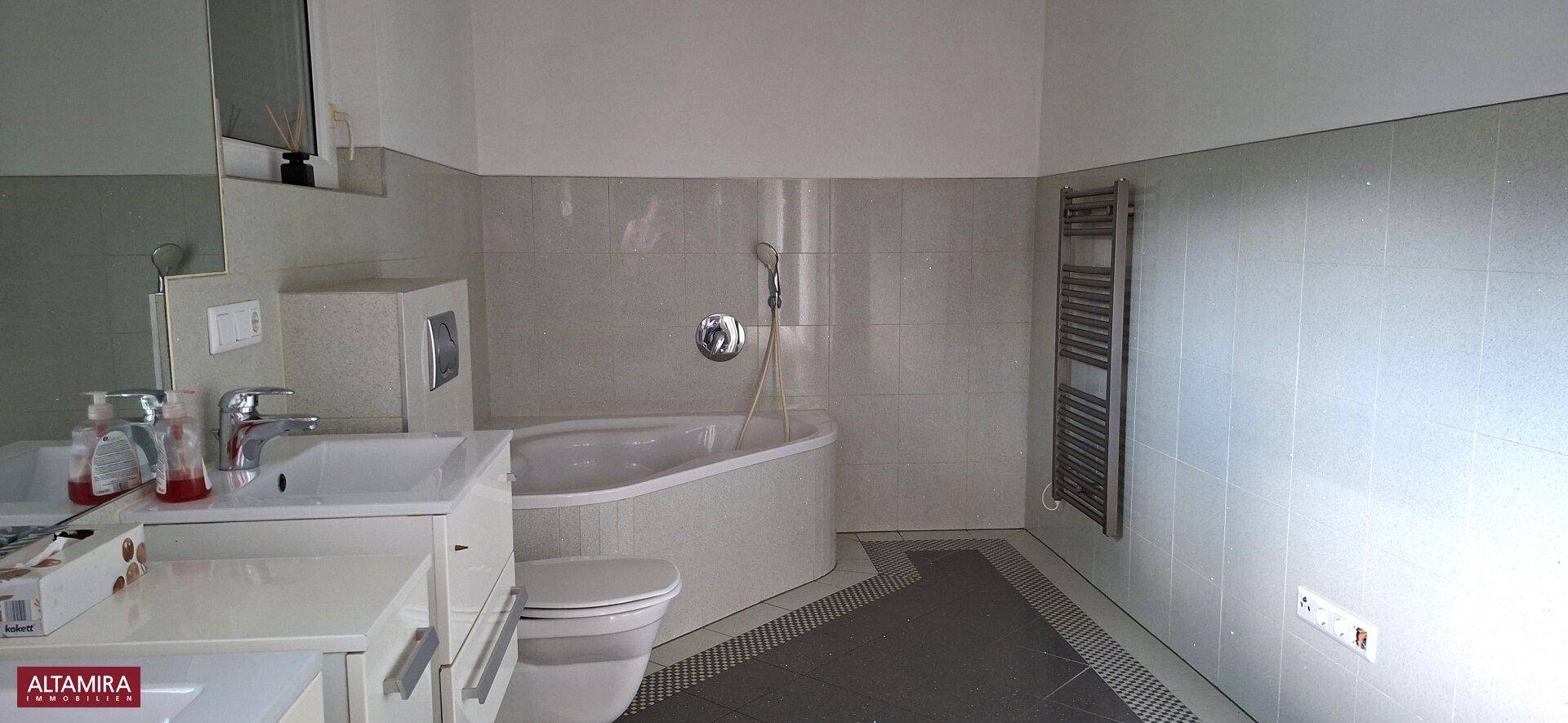 Helles Badezimmer mit Badewanne, WC, Einzelwaschbecken und beheiztem Handtuchhalter in modernem Design.