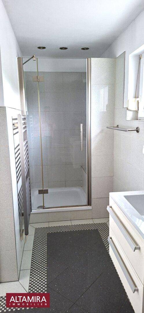 Modernes Badezimmer mit Duschkabine, beheiztem Handtuchhalter und dunklen Bodenfliesen.