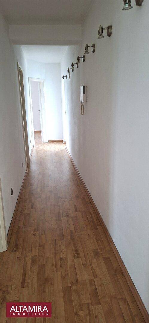 Langer Flur mit Holzboden und weiß gestrichenen Wänden, der zu weiteren Räumen führt.